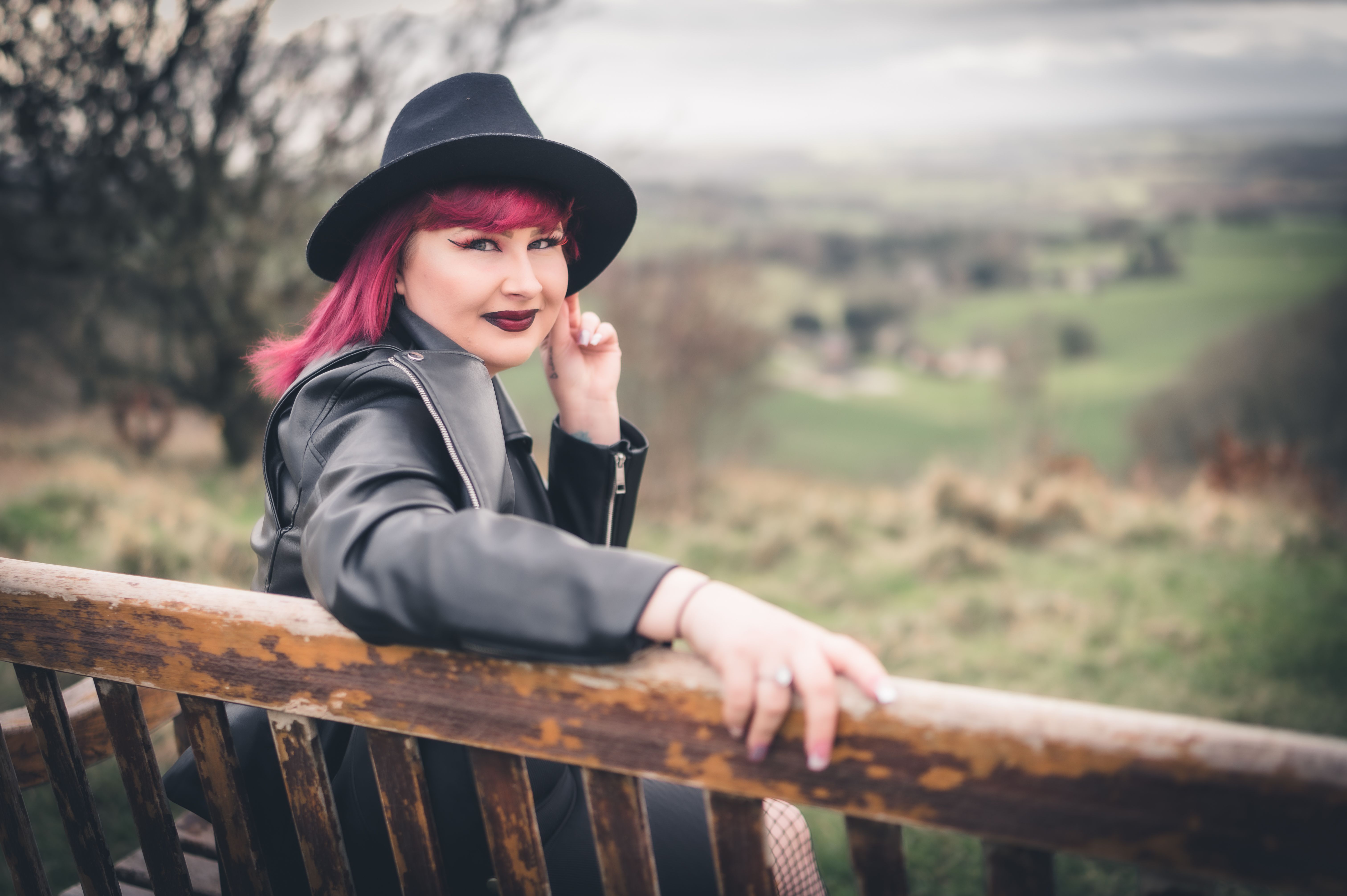 Stylish woman with pink hair and black hat sitting on a bench outdoors in Dursley, England
