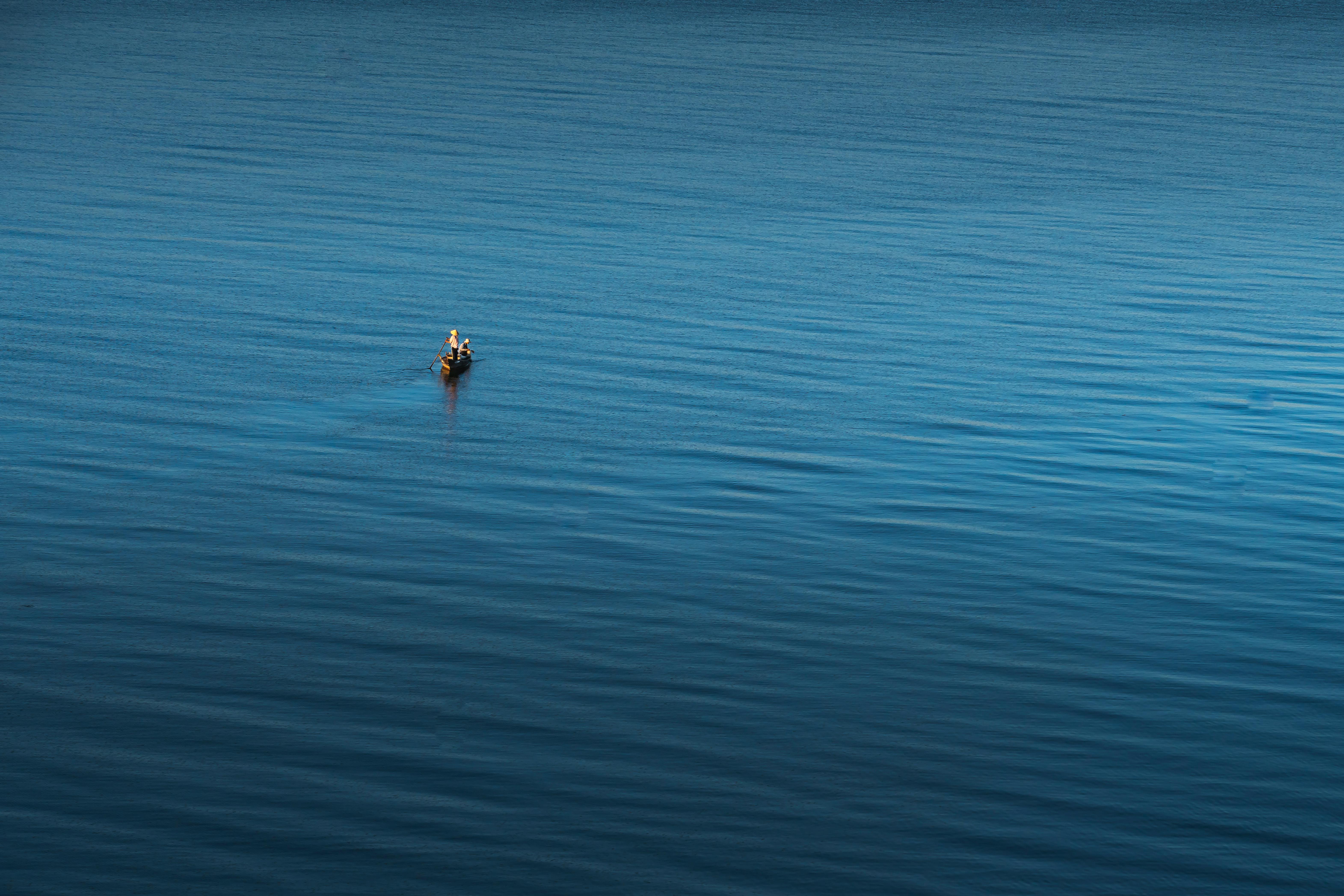 广阔的蓝色水域中，一位孤独的渔夫在小船上，唤起孤独与宁静