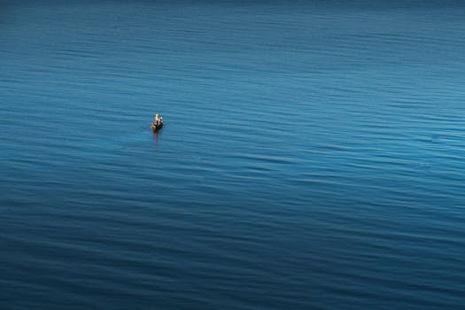 广阔的蓝色水域中，一位孤独的渔夫在小船上，唤起孤独与宁静