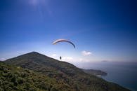 阳光明媚的晴朗日子里，滑翔伞飞越郁郁葱葱的山地，背景是海洋