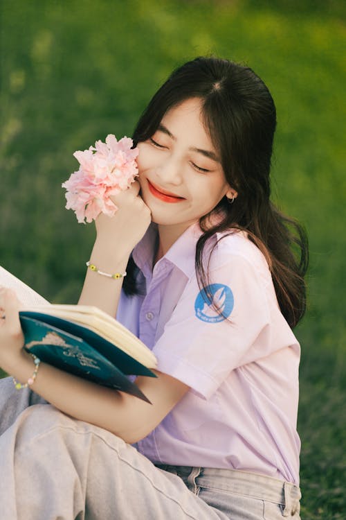 Cute Brunette Woman Reading Book While Holding Pink Flowers in Hand