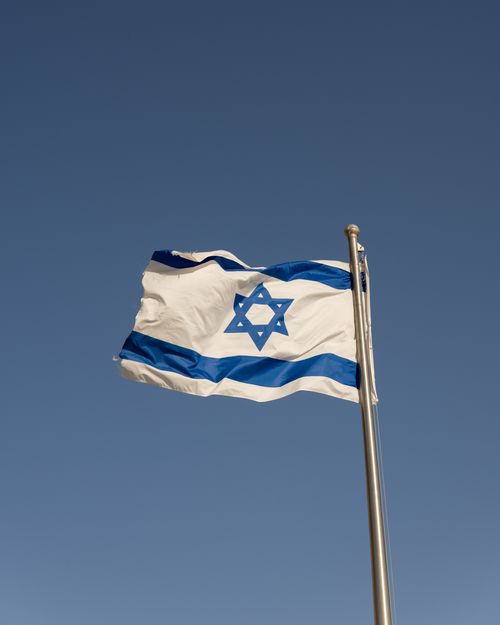 Free A vibrant Israeli flag on a flagpole waving against a clear blue sky in Jerusalem. Stock Photo