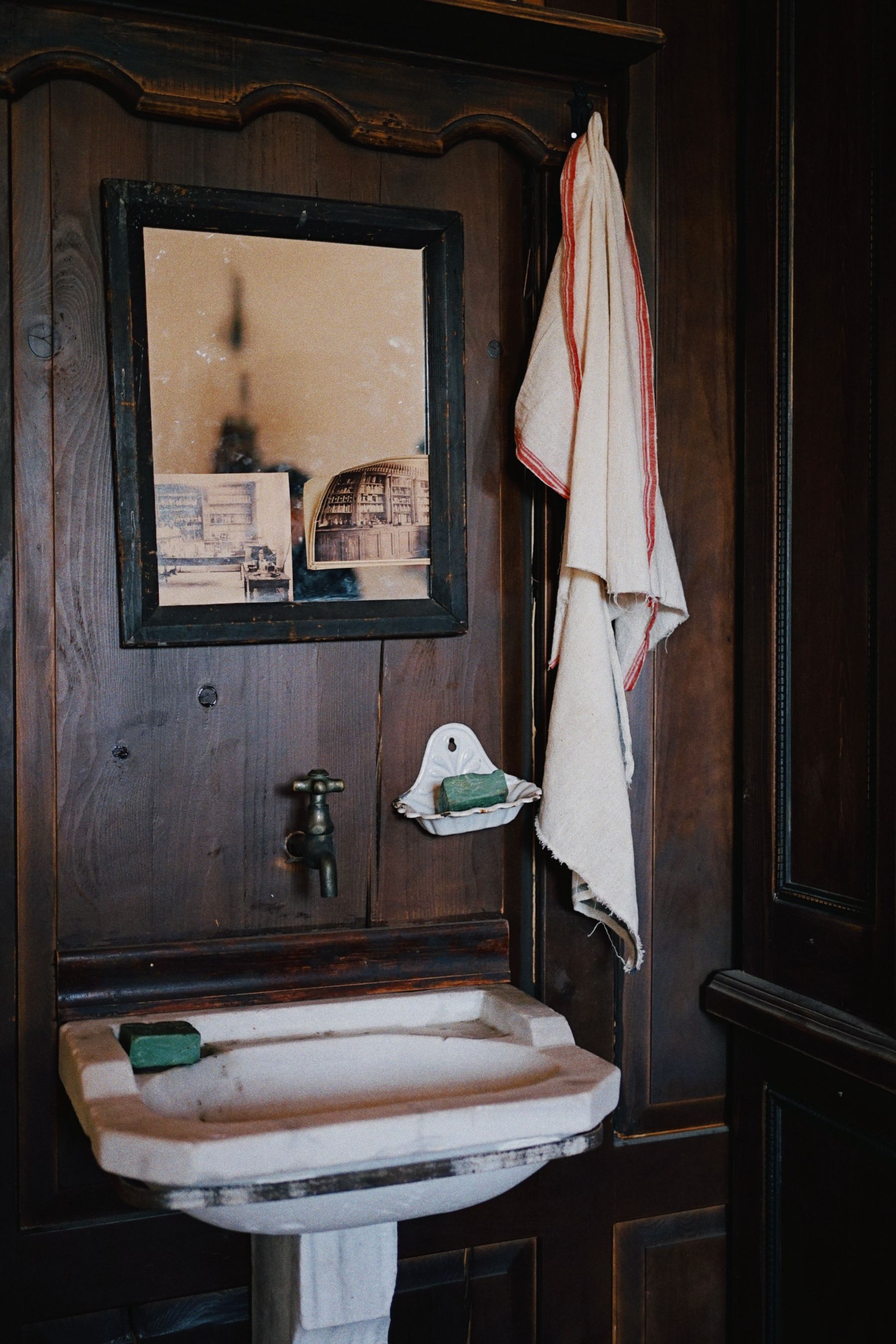 Aged timber washstand with a white vessel basin and framed mirror in a rustic vintage bathroom