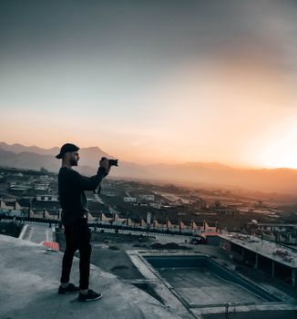 A man captures a stunning sunset on a rooftop with mountains in the background.