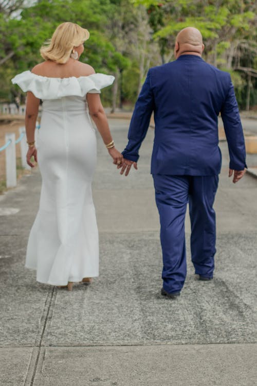 A man and woman in white dresses walking down a sidewalk