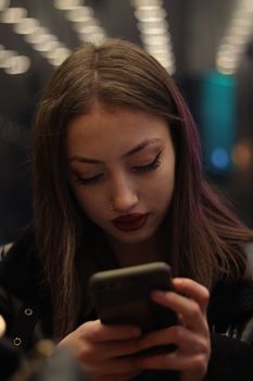 A young woman focused on her smartphone amidst city lights at night, creating a moody ambience.