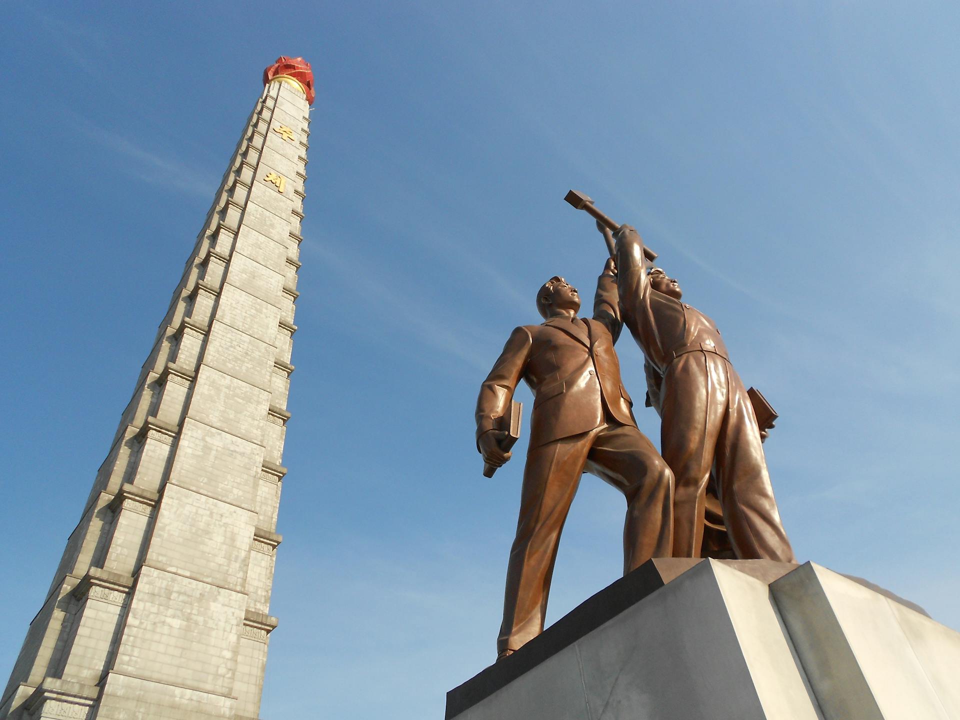 Low angle view of Juche Tower and worker statues against a clear blue sky in Pyongyang, North Korea.