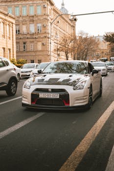 A sleek white car navigates a bustling city street in the afternoon.