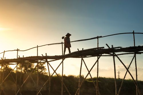 Free A solitary figure walks on a rustic wooden bridge during a stunning sunset, highlighting the beauty of nature and simplicity. Stock Photo
