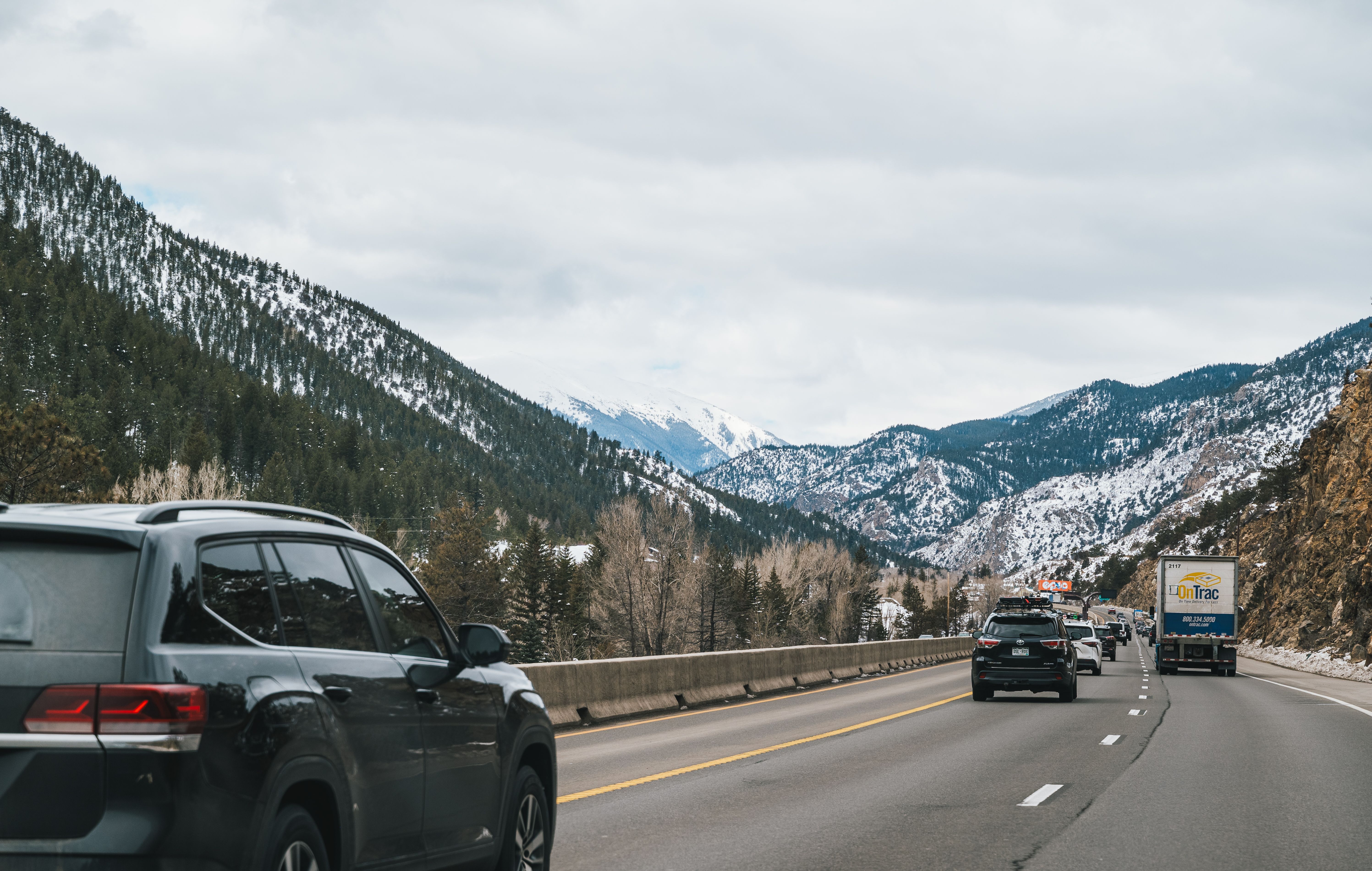 Cars driving on a scenic snowy highway with mountain views in winter.