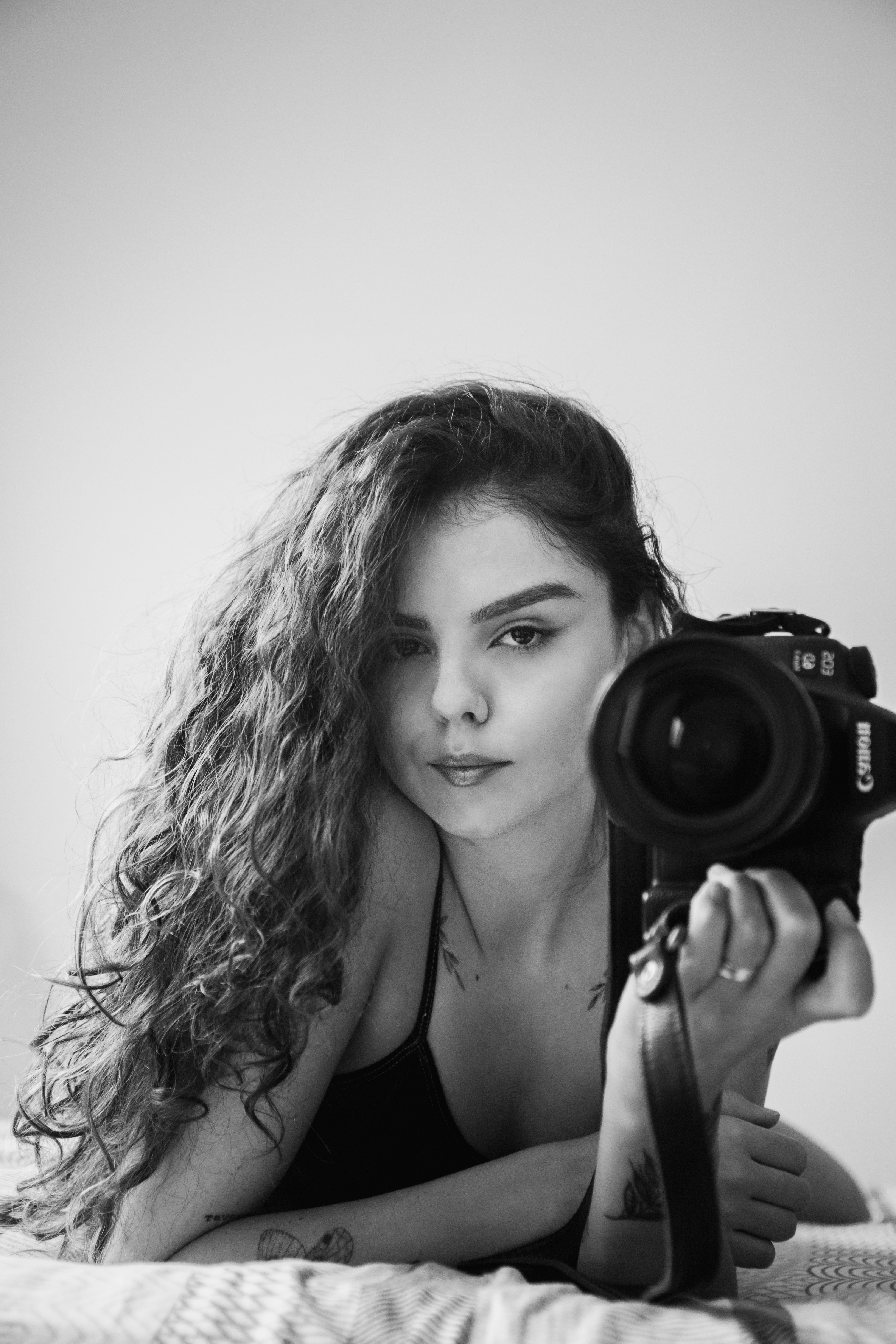 Artistic black and white portrait of a woman holding a camera, featuring natural lighting.