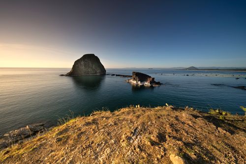 Free Stunning view of a rocky island at sunset with clear skies and a serene ocean, perfect for travel inspiration. Stock Photo