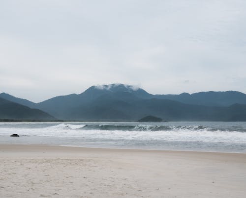A person standing on the beach with mountains in the background