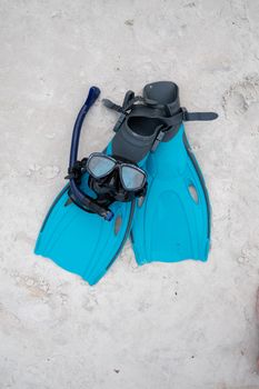 Close-up of snorkeling gear including fins and mask on sandy shore.