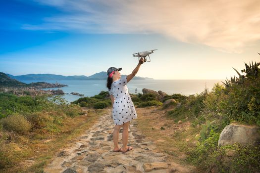 A woman in a polka dot dress launches a drone on a scenic coastal path during the day, capturing beautiful vistas.
