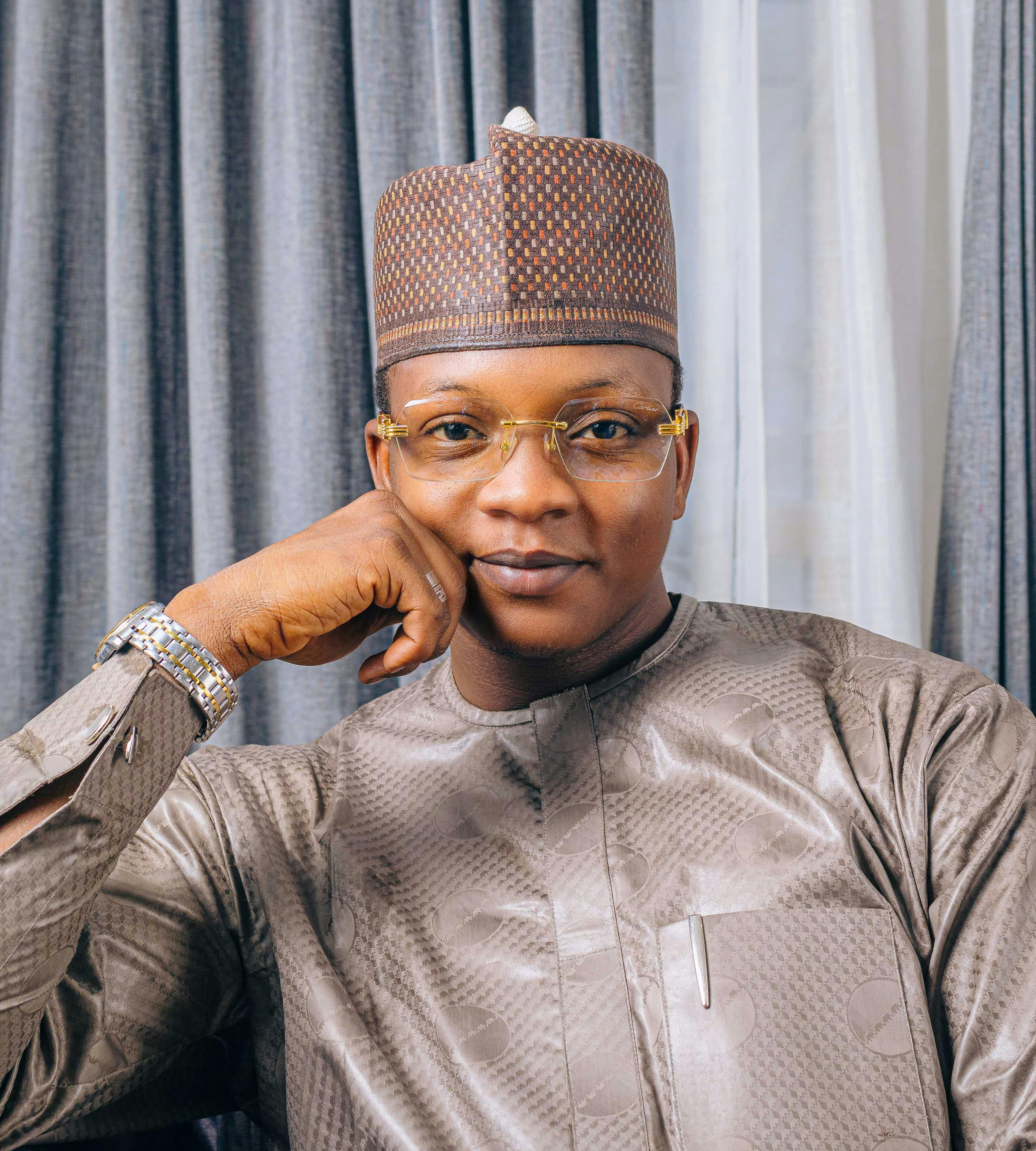 Portrait of a smiling man wearing traditional attire and glasses indoors.