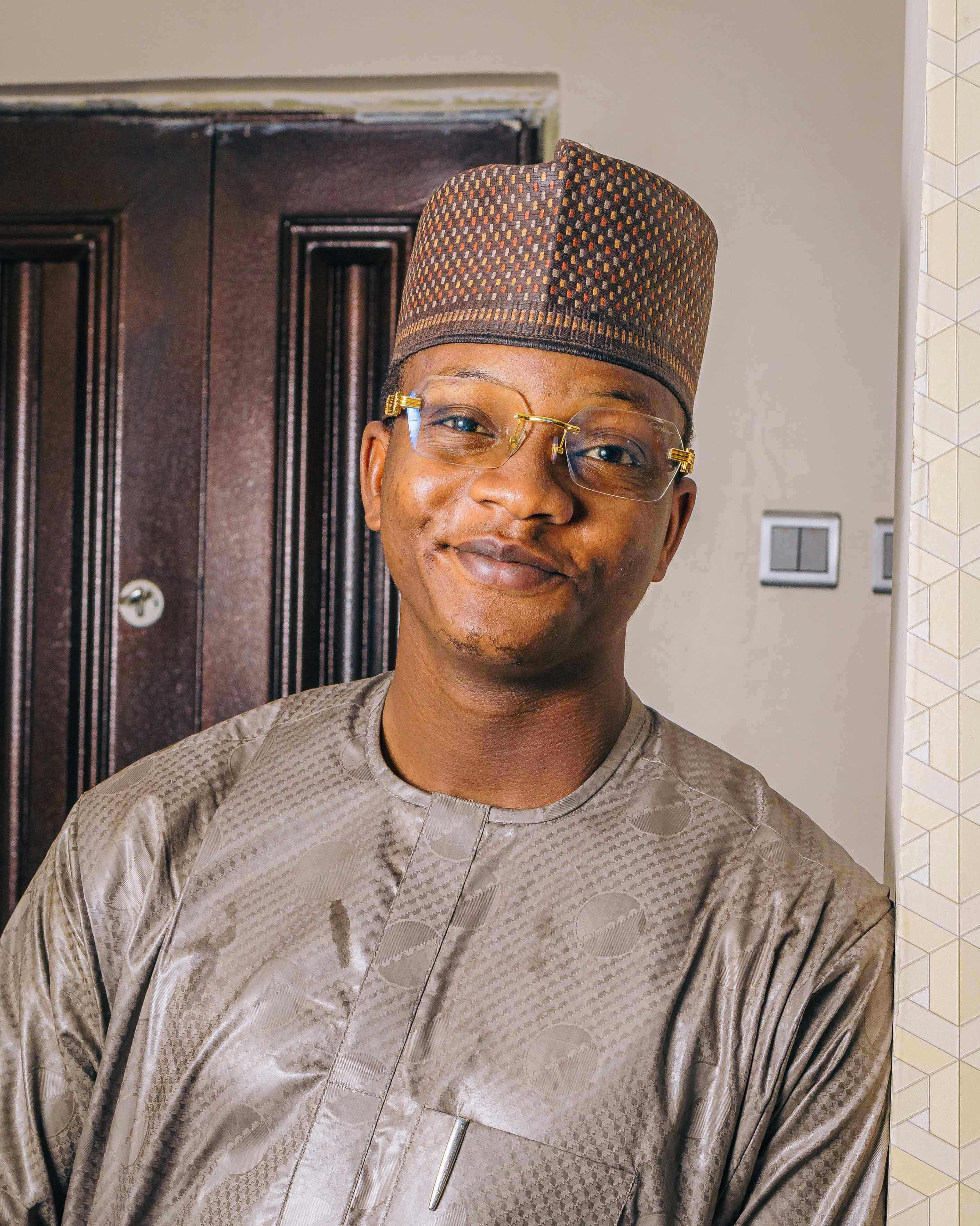 A smiling man wearing traditional clothing and glasses indoors.