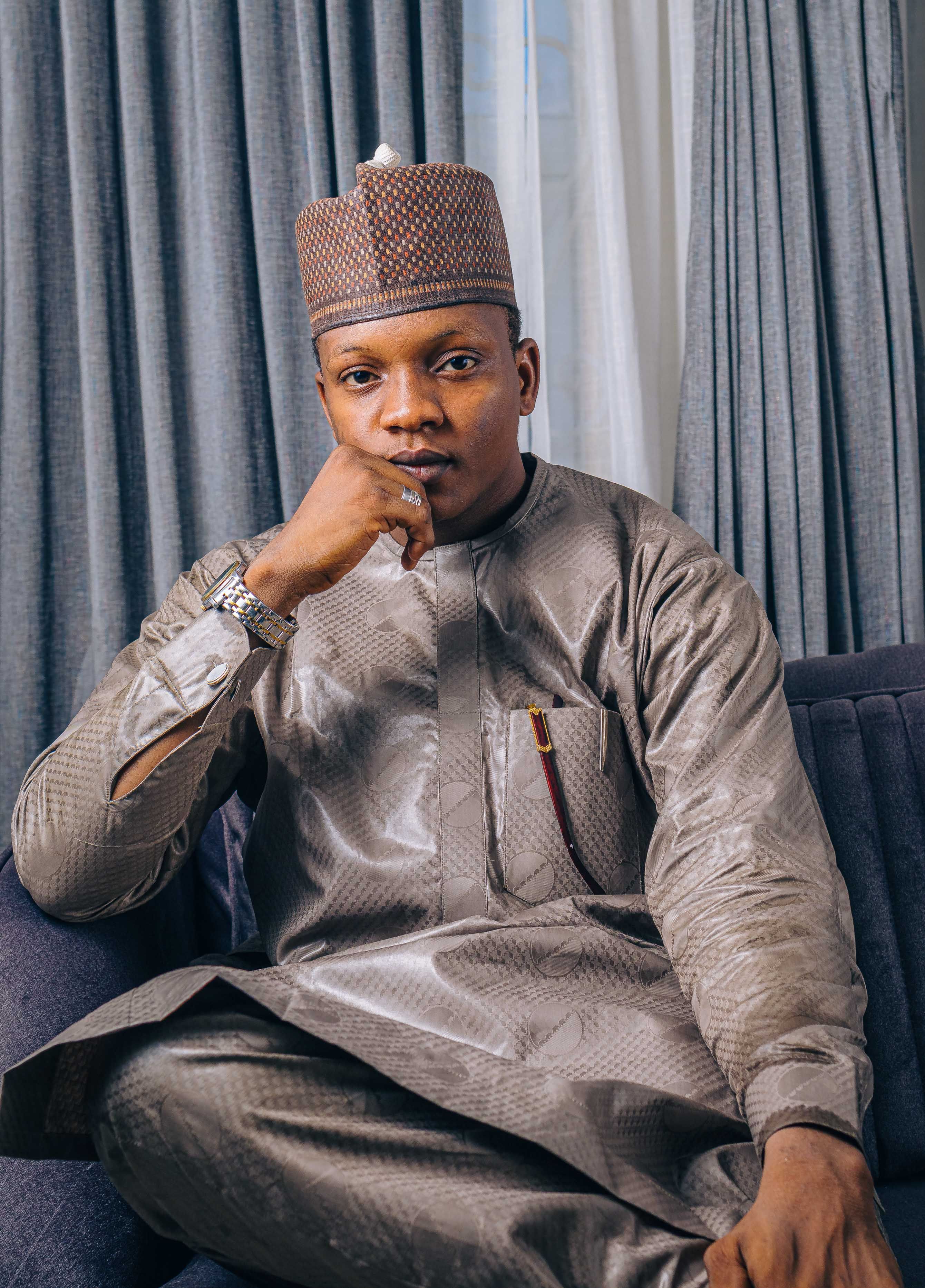 Portrait of a seated man in traditional attire, featuring a stylish kufi hat and kurta.