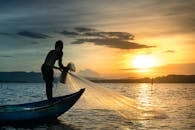 日出时分，渔夫在宁静的湖面上撒网的剪影