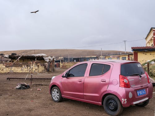 A pink car parked in front of a dirt road