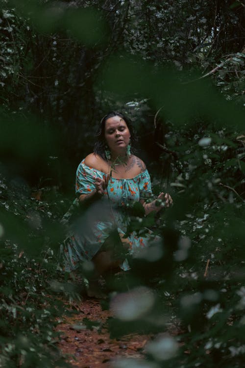 A woman in a blue dress is sitting in the woods