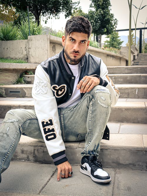 A man in a baseball jacket sitting on some steps