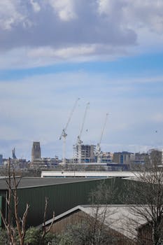 Cityscape view of construction cranes against a clear blue sky, symbolizing urban development.