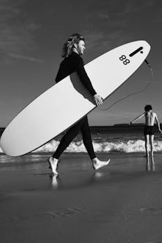 Surfer walking with surfboard at Sydney beach, capturing active lifestyle in black and white.