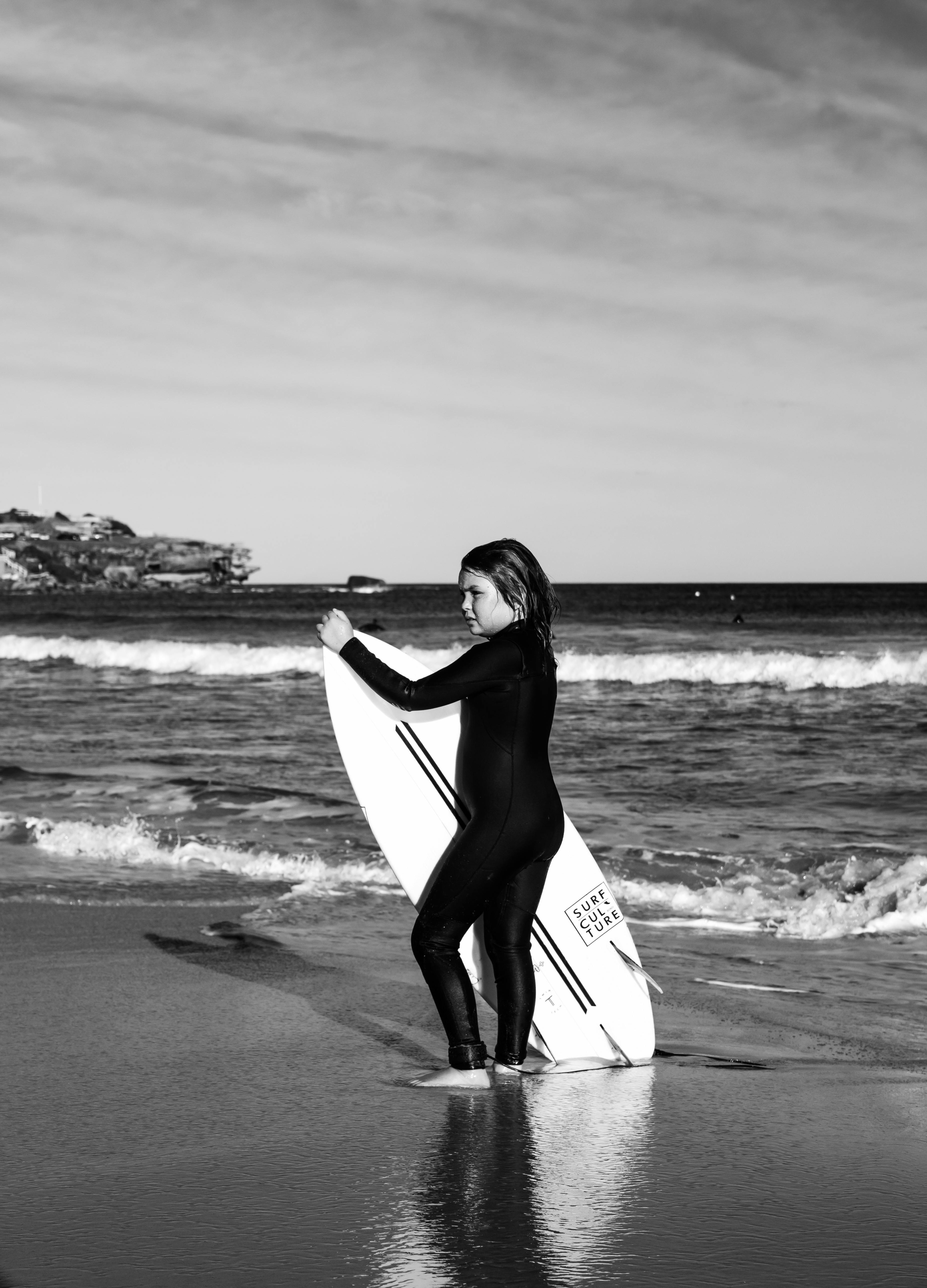Child surfer standing with surfboard on Sydney beach in black and white. Summer vacation vibe.