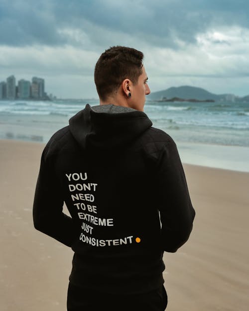 A man standing on the beach wearing a hoodie that says you don't have to be a zombie