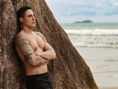 A shirtless man leaning against a rock by the ocean