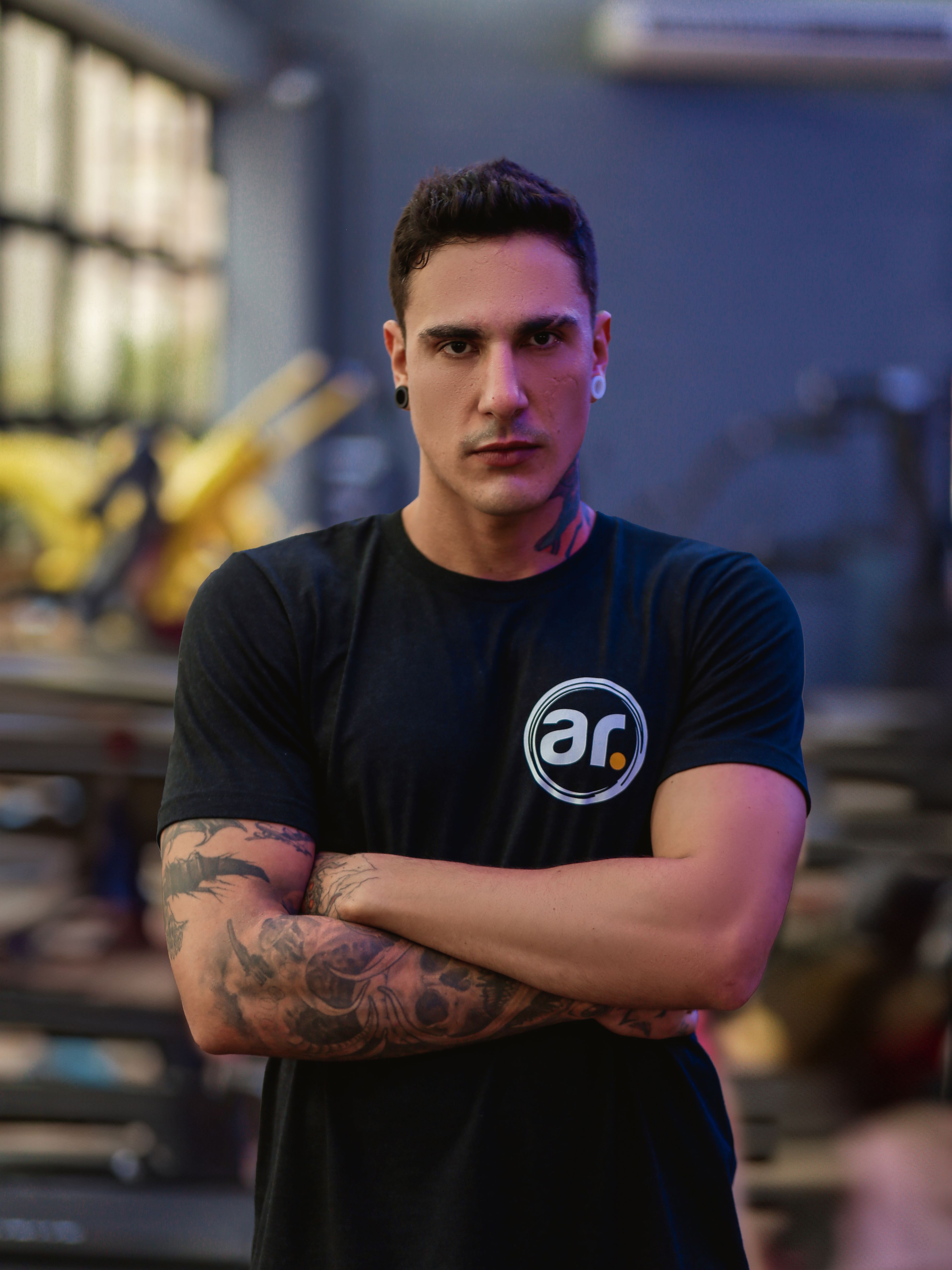 Portrait of a tattooed man in a gym wearing a black t-shirt, conveying strength and confidence.