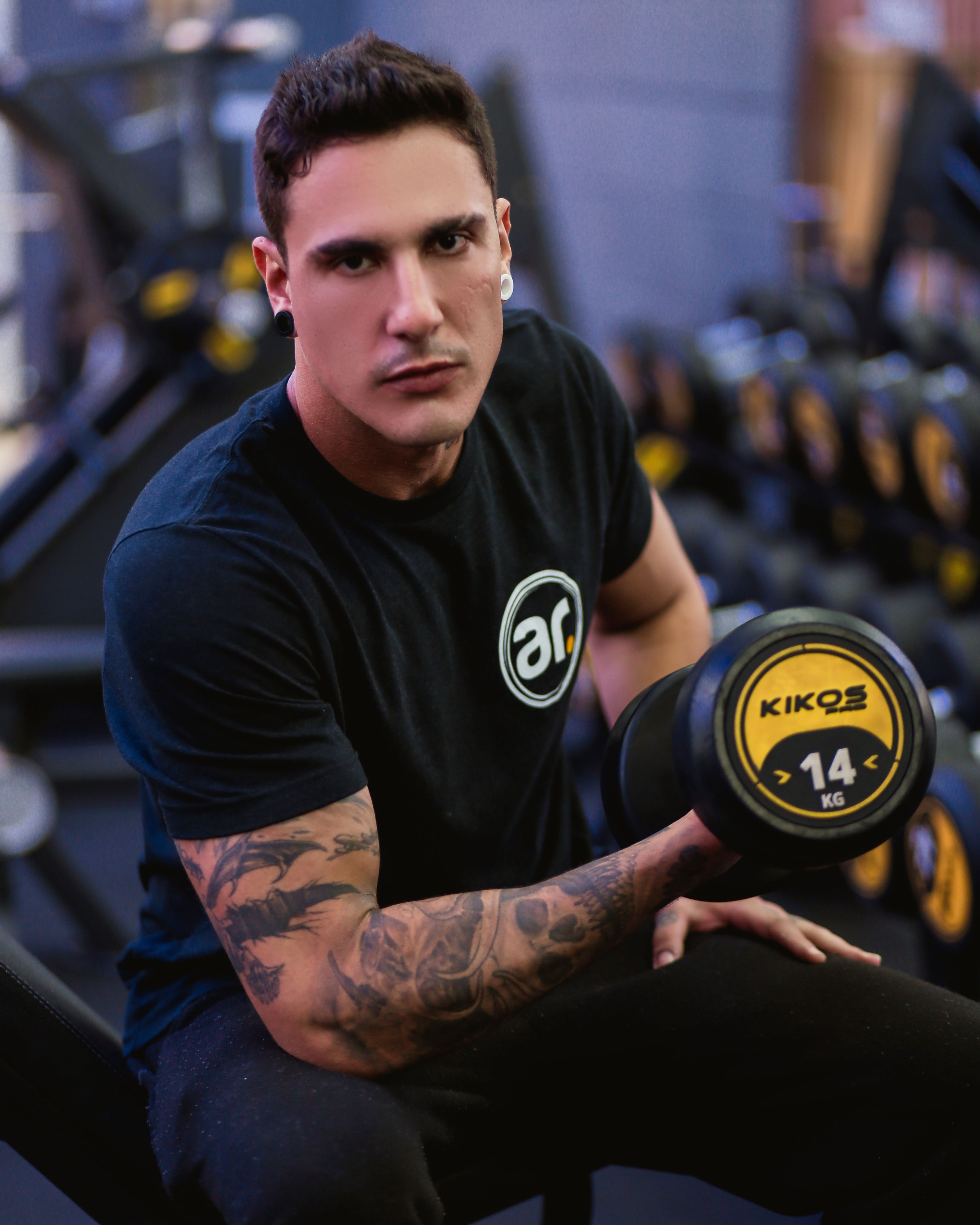 Focused man lifting a 14 kg dumbbell inside a gym, showcasing strength and dedication.