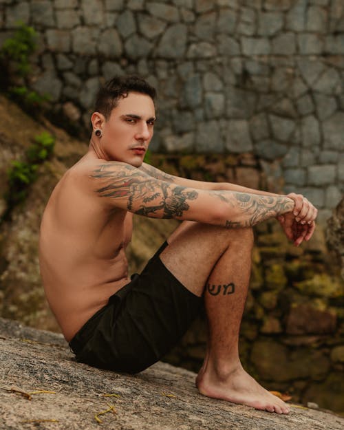 A man with tattoos sitting on a rock