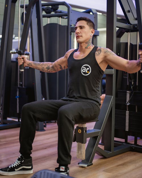 A man in a black tank top is doing exercises in a gym