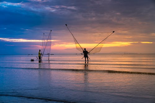 Photo of Two Men Holding Nets in Ocean