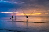 日出时分，两名渔民在宁静的海面上撒网，营造出一片宁静的景象