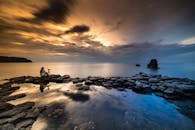 一位孤独的摄影师在岩石海岸，捕捉到了映照在平静海面上的日落
