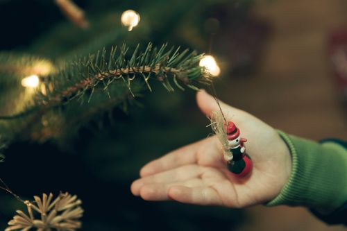 Free A close-up of a child placing a snowman ornament on a Christmas tree branch with lights. Stock Photo