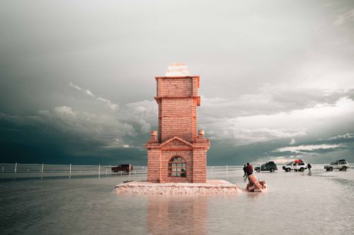 Free Photography of a striking tower in the vast Salar de Uyuni salt flat in Bolivia, with vehicles and a reflective surface. Stock Photo