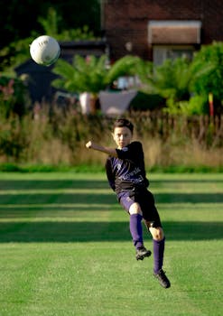Dynamic shot of a young boy playing soccer and kicking a ball in a grassy field.