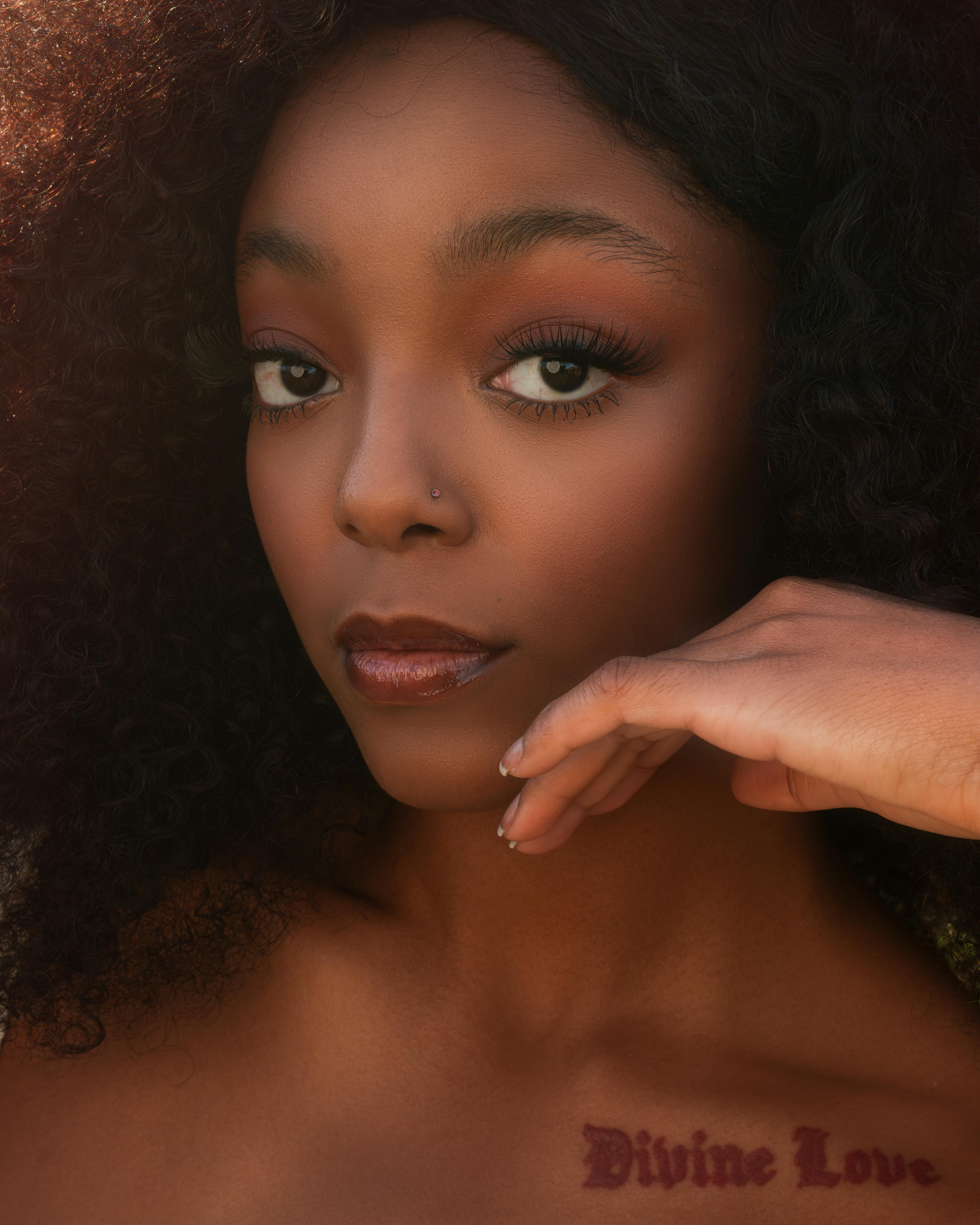 Close-up portrait of a young Black woman with a tattoo, showcasing elegance and confidence.