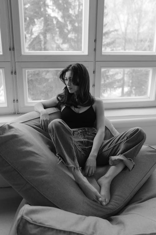 Woman Sitting on Pillow near Windows in Black and White