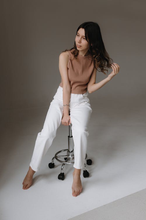 Free A woman sitting on a stool in a white top and white pants Stock Photo