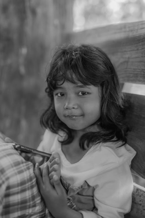 Free A black and white photo of a little girl sitting on a bench Stock Photo