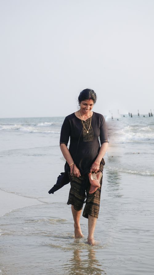 Free A woman in a black dress enjoys a peaceful walk along the ocean shore. Stock Photo