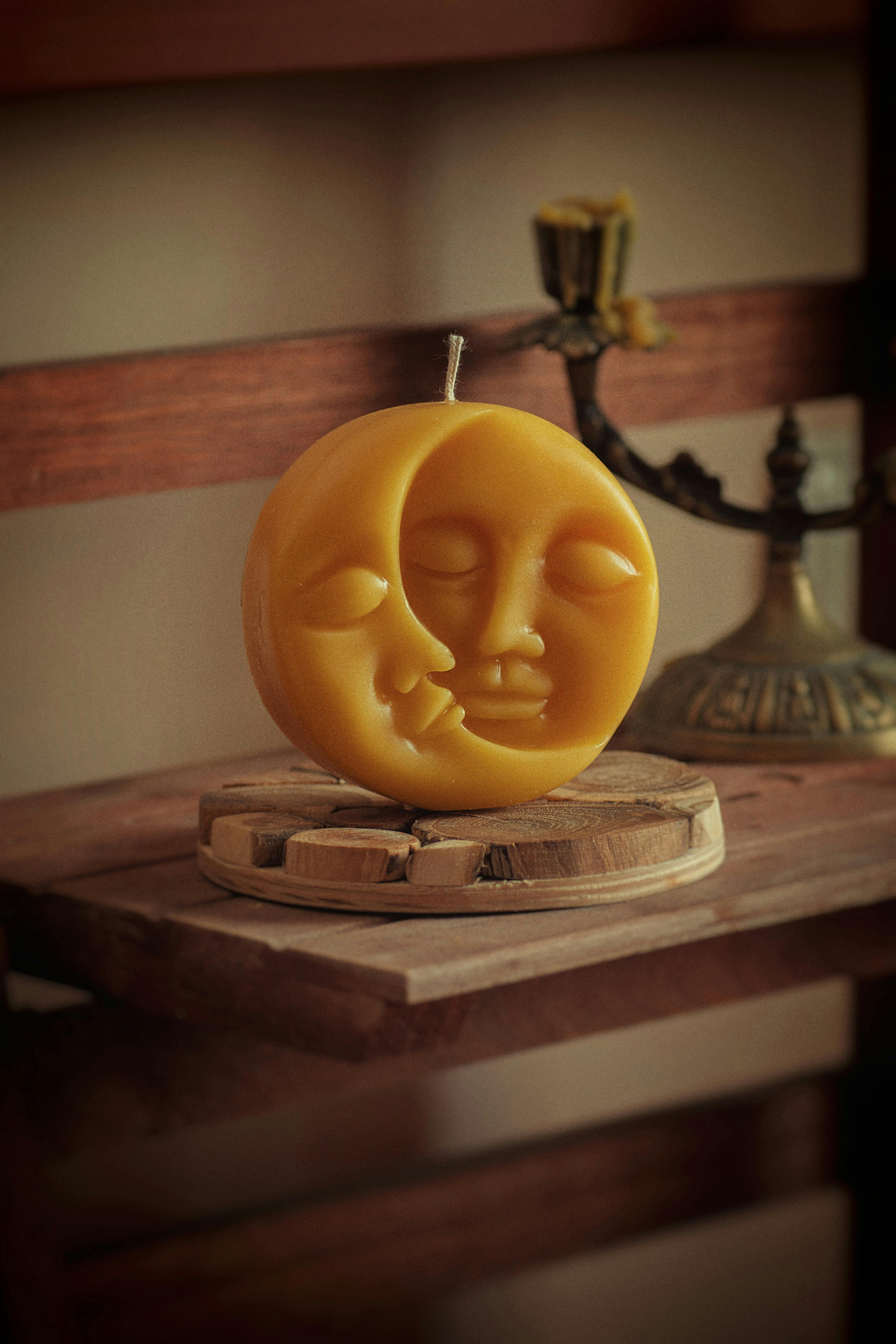 A decorative candle shaped like a moon face resting on a wooden tray, captured in a cozy setting.