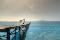 一名妇女拿着一条彩虹色围巾，站在木码头上，映衬着大海