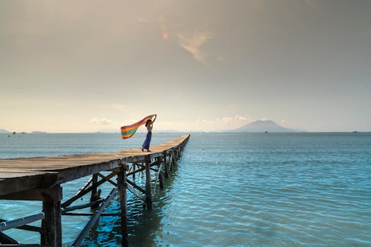 一名妇女拿着一条彩虹色围巾，站在木码头上，映衬着大海