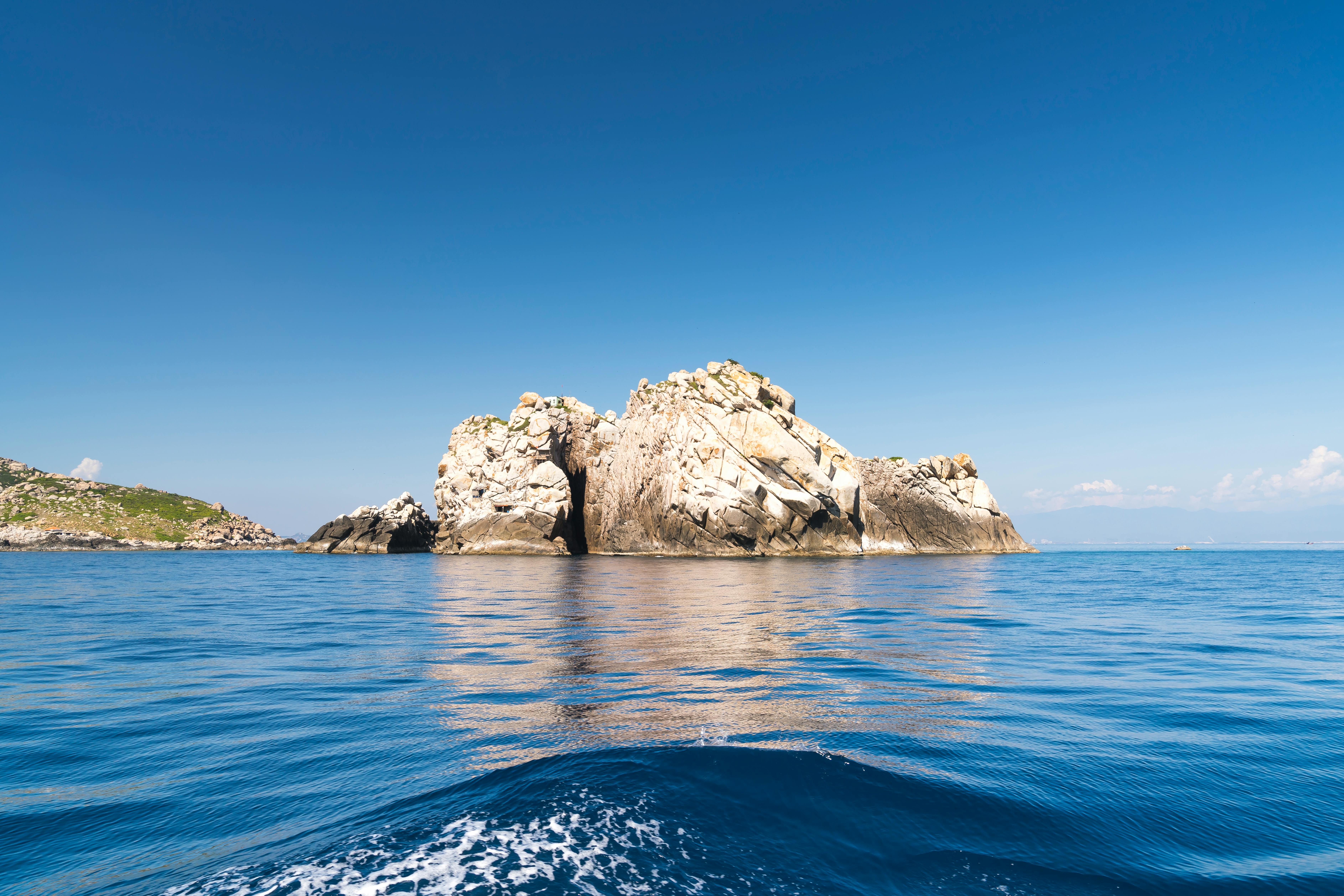 蔚蓝的天空下，一座岩石岛屿宁静地矗立，四周环绕着平静的海水